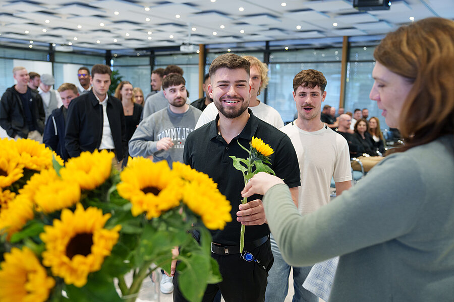 Gruppe von jungen Menschen, die von einer Frau Blumen überreicht bekommen