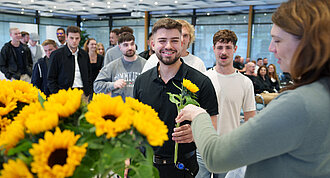 Gruppe von jungen Menschen, die von einer Frau Blumen überreicht bekommen