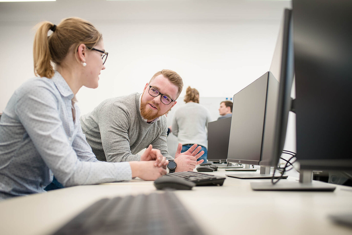 Zwei Auszubildende sitzen in einem Computerraum und schauen sich an.