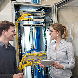 Zwei Auszubildende stehen sich gegenüber und sprechen miteinander vor einer technischen Umgebung.