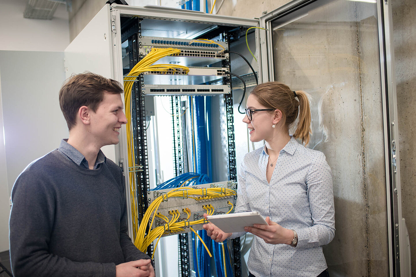 Zwei Auszubildende stehen sich gegenüber und sprechen miteinander vor einer technischen Umgebung.